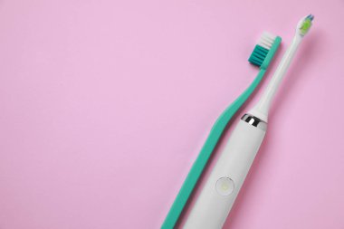 Pembe arka planda elektrikli ve plastik diş fırçaları. Metin için boşluk