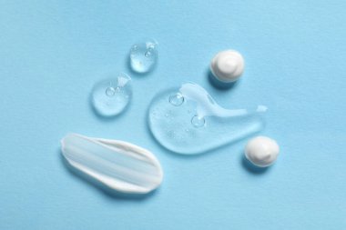 Açık mavi zemin üzerinde şeffaf jel ve beyaz krem örnekleri, düz yatıyordu