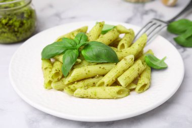 Pesto soslu lezzetli makarna ve beyaz mermer masada fesleğen, yakın plan.