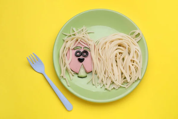 Creative serving for kids. Plate with cute dog made of tasty pasta, sausage and cucumber on yellow table, flat lay