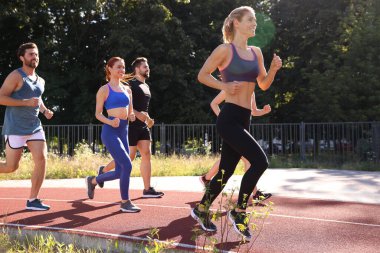 Güneşli bir günde stadyumda koşan bir grup insan