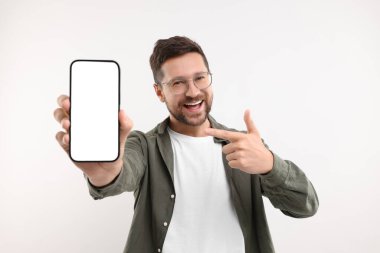 Yakışıklı bir adam elinde akıllı telefon gösteriyor ve beyaz arka planda onu işaret ediyor.