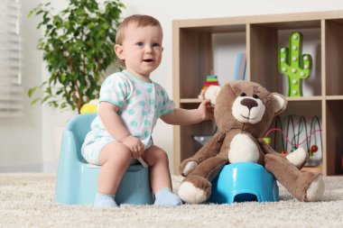 Küçük çocuk ve oyuncak ayı içeride plastik bebek tuvaletlerinde oturuyorlar.