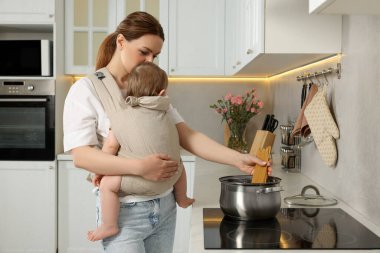 Anne, mutfakta makarna pişirirken çocuğunu askıda tutuyor.