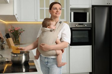 Anne, mutfakta makarna pişirirken çocuğunu askıda tutuyor.