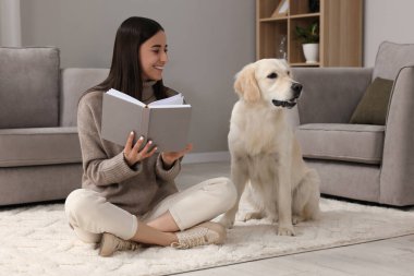 Evde yerde sevimli Labrador Retriever köpeğiyle kitap okuyan mutlu kadın. Sevimli hayvan.