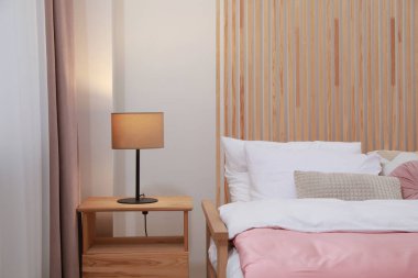 Yatak odasındaki ahşap komodinin üzerinde yastıkları ve lambaları olan rahat bir yatak. İç tasarım