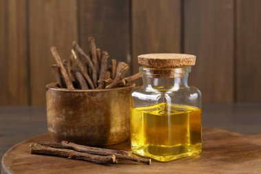 Kurumuş meyan kökü çubukları ve ahşap tahtada gerekli yağ, yakın plan.