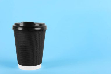 Açık mavi zemin üzerinde plastik kapaklı siyah kağıt bardak, metin için boşluk. Kahve hazır.