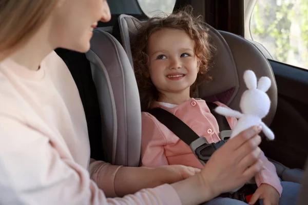Nettes Kleines Mädchen Sitzt Kindersitz Neben Mutter Mit Spielzeugkaninchen Auto — Stockfoto