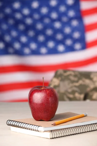 Notebooks, apple and pencil on light table against flag of USA. Military education