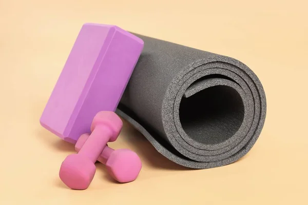 Grey exercise mat, yoga block and dumbbells on beige background
