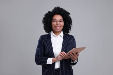 Gri arka planda tableti olan genç bir iş kadını