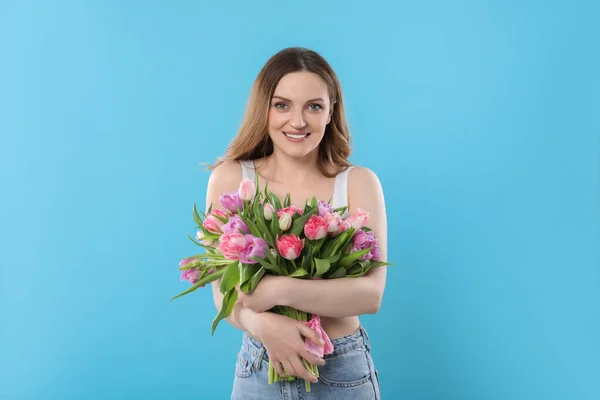 ライトブルーの背景に美しいチューリップの花束を持つ幸せな若い女性 — ストック写真