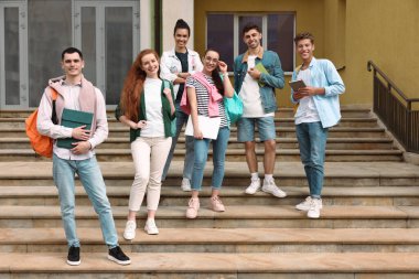 Bir grup mutlu genç öğrenci dışarıda birlikte vakit geçiriyorlar.