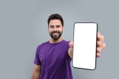 Açık gri arka planda akıllı telefon gösteren genç adam