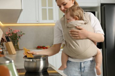 Anne, mutfakta makarna pişirirken çocuğunu askıda tutuyor.