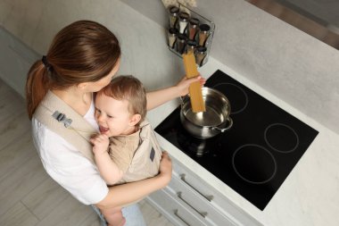 Anne çocuğunu askıda tutarken (bebek taşıyıcısı) içeride makarna pişirirken, yukarıdan bakıldığında