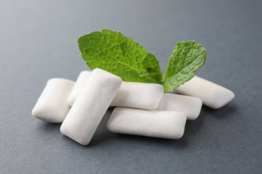 Tasty white chewing gums and mint leaves on grey background, closeup clipart