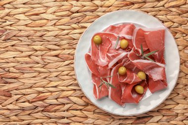 Hasır hasırın üzerinde lezzetli jambon, zeytin ve biberiye dilimleri. Metin için boşluk