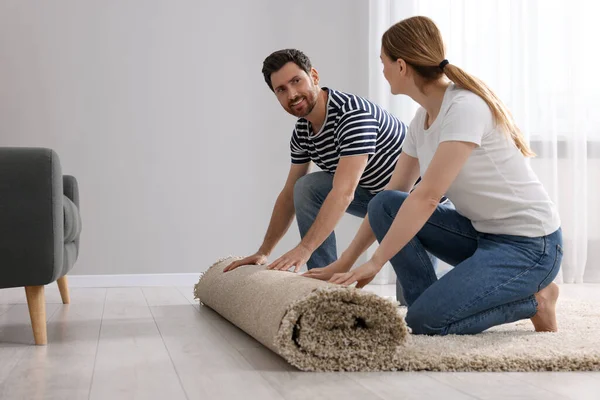 Smiling couple unrolling carpet on floor in room