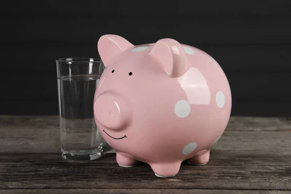 Water scarcity concept. Piggy bank and glass of drink on wooden table
