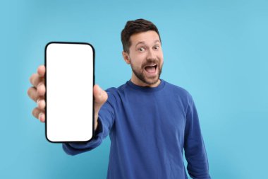 Açık mavi arka planda elinde akıllı telefon gösteren şaşırtıcı bir adam.