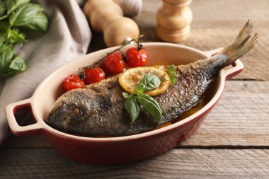 Domatesli, fesleğenli ve limonlu Dorado balığı ahşap masada, yakın plan.