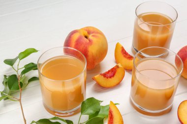 Bir bardak şeftali suyu, taze meyve ve yapraklar beyaz ahşap masada.