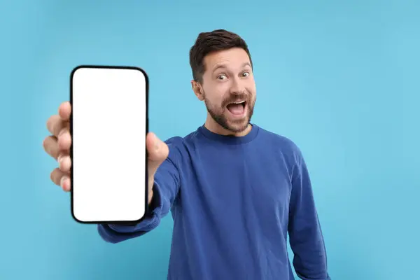 stock image Surprised man showing smartphone in hand on light blue background