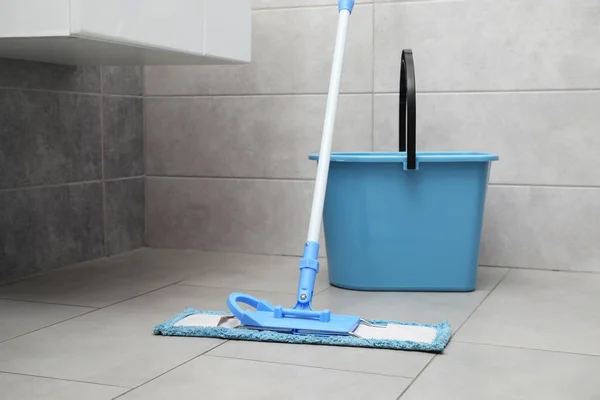 Mop and bucket on tiled floor in toilet