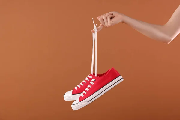 Kahverengi Arka Planda Bir Çift Kırmızı Klasik Spor Ayakkabı Tutan — Stok fotoğraf