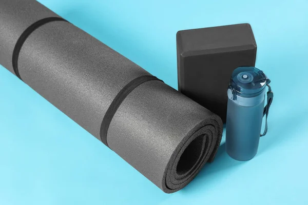 Exercise mat, yoga block and bottle of water on light blue background