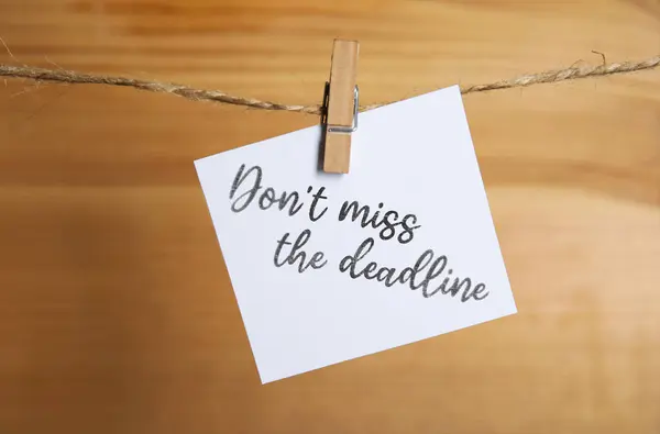 Note with reminder Don\'t Miss The Deadline hanging on twine against wooden background