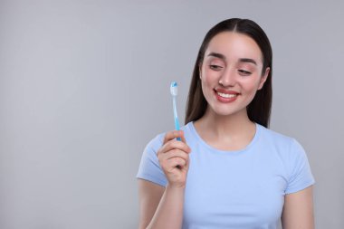 Açık gri arkaplanda plastik diş fırçası tutan mutlu genç kadın, metin için boşluk