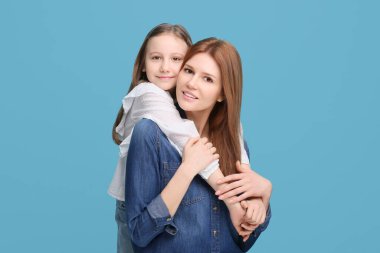 Açık mavi arka planda mutlu anne ve tatlı kızının portresi.