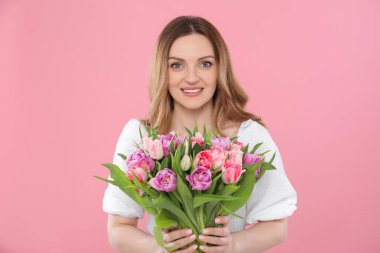 Pembe arka planda güzel lalelerle dolu buketi olan mutlu genç bir kadın.
