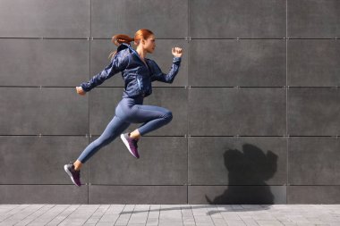 Spor elbiseli güzel bir kadın sokakta koyu gri duvarın yanında zıplıyor, mesaj atmak için yer var.