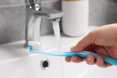 Banyoda lavabonun üzerinde akmakta olan suyun yanında plastik diş fırçası tutan kadın, yakın plan.