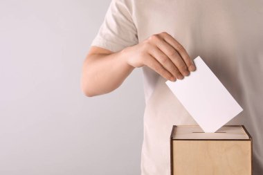 Adam oyunu açık gri arka planda oy sandığına koyuyor, yakın plan. Metin için boşluk
