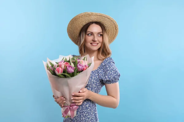 ライトブルーの背景に美しいチューリップの花束を保持するわら帽子で幸せな若い女性 — ストック写真