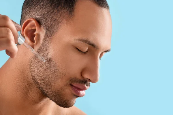 stock image Handsome man applying cosmetic serum onto face on light blue background, closeup. Space for text