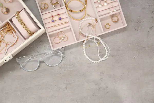 Jewelry boxes with many different accessories and glasses on light grey table, flat lay. Space for text