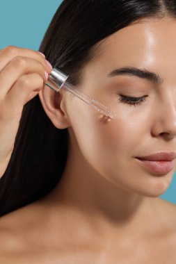Güzel genç bir kadın yüzüne serumu uyguluyor açık mavi arka planda, yakın plan