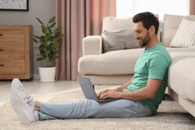 Evdeki kanepenin yanında dizüstü bilgisayar kullanan bir adam.