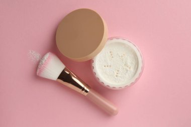 Pembe arka planda gevşek yüz pudrası ve makyaj fırçası.