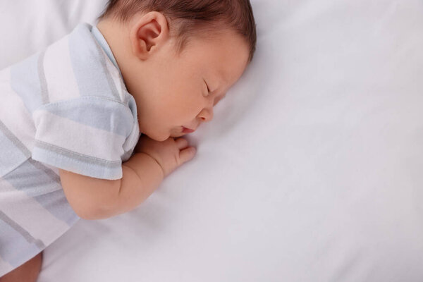 Милый новорожденный ребенок спит на белой кровати, вид сверху. Пространство для текста