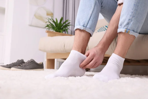 Man putting on white socks at home, closeup. Space for text