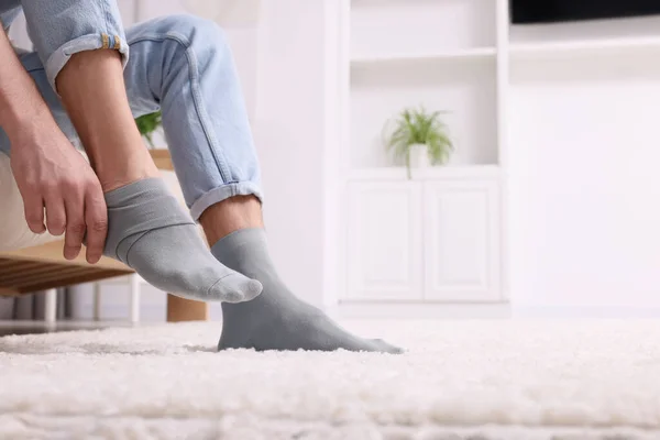 Man putting on grey socks at home, closeup. Space for text