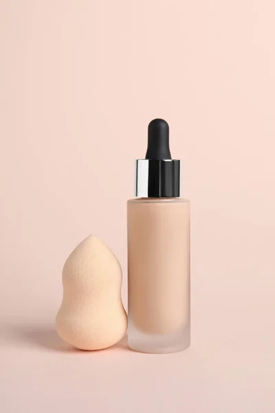 Bottle of skin foundation and sponge on beige background. Makeup product